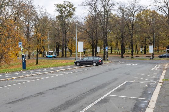 Eine asphaltierte Straße am Heinrich-Heine-Platz mit einem parkenden Auto im Herbst mit gelbem Laub.